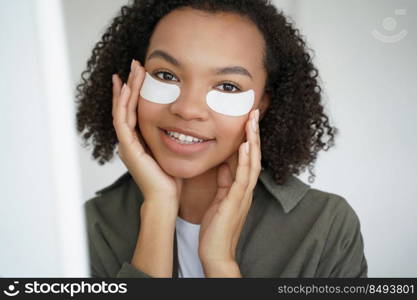 Anti wrinkle procedure. Happy afro girl is applying eye patches. Skin moisturizing and nourishing with collagen. Beauty routine of teenage girl. Morning skincare of young lovely hispanic woman.. Anti wrinkle procedure. Happy afro girl is applying eye patches. Skincare of hispanic young woman.