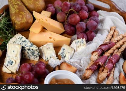 Antipasto. Dish with crispy grissini wrapped in sun-dried bacon, slices of brie cheese, camembert, blue cheese, radamer and muscat grape vine with fruit.