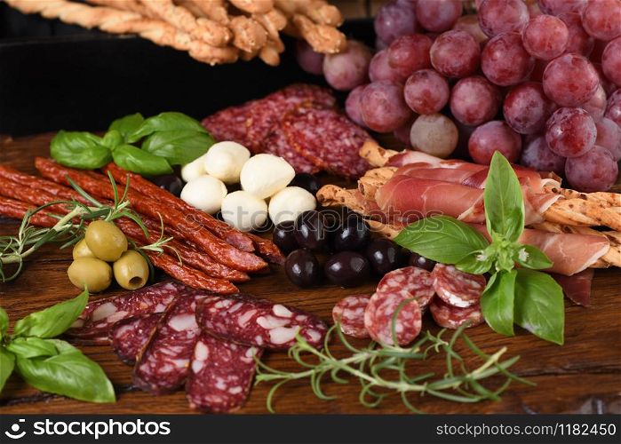 Antipasto. Dish with sausage, dried ham, salami, crispy grissini with grapes. A meat appetizer is a great idea