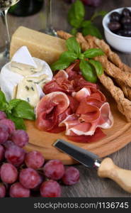 Antipasto. Wine set snacks of dried ham, brie cheese with mold, parmesan with grissini, olives and pink grapes.