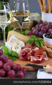 Antipasto. Wine set snacks of dried ham, camembert cheese with mold, parmesan with grissini, olives and pink grapes.