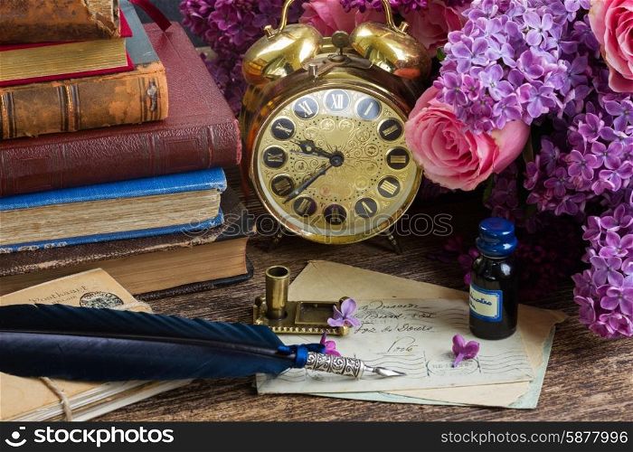 antique alarm clock, pile of mail with blue feather pen and flowers