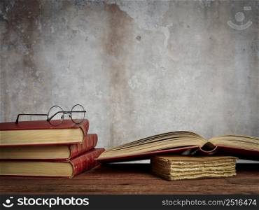 antique books and reading glasses on a rustic wooden table with a grunge wall background