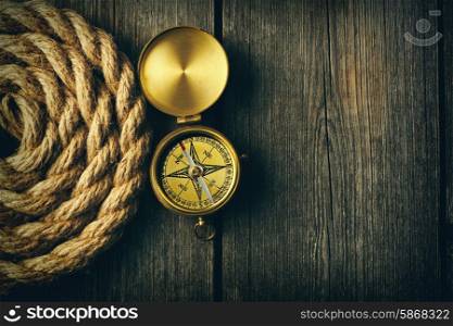 Antique brass compass and rope over wooden background