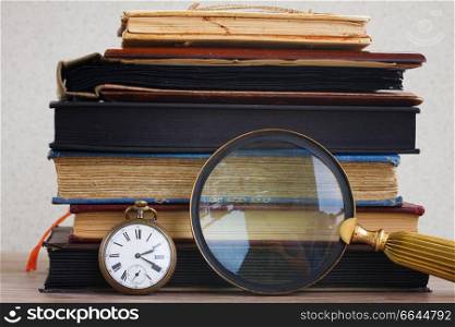 antique clock with loupe  on pile of  vintage books background