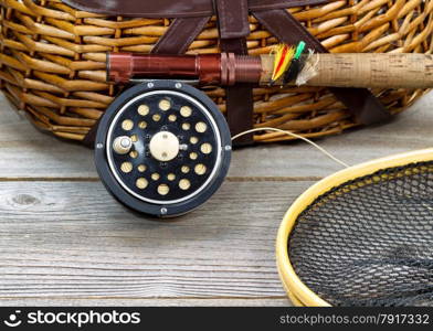 antique fly fishing reel, rod, landing net, creel and artificial flies on rustic wood. Layout in horizontal format.