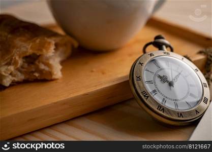 Antique gold pocket watch placed on the side of the wooden tray With a white coffee mug And the pie that has been bitten