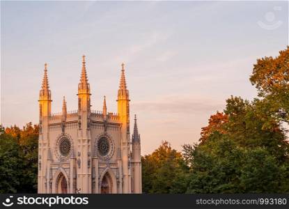 Antique gothic chapel in the park on a background of autumn trees and sky. Antique gothic chapel lit by the rays of the sun against the blue sky