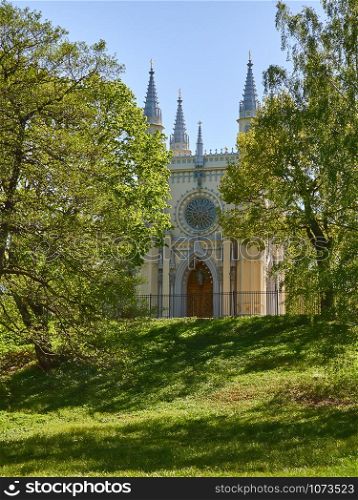 Antique gothic chapel in the park on a background of trees and sky. Antique gothic chapel lit by the rays of the sun against
