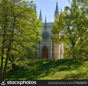 Antique gothic chapel in the park on a background of trees and sky. Antique gothic chapel lit by the rays of the sun against