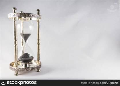 Antique hourglass, black sand, textured background. Left of image, blank space on right , landscape, top half running out.