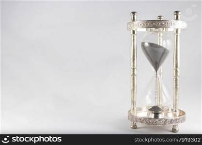 Antique hourglass, black sand, textured background. Right of image, blank space on left, landscape, top half almost full.