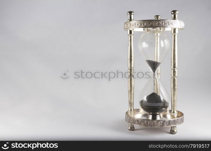 Antique hourglass, black sand, textured background. Right of image, blank space on left, landscape, top half almost empty.