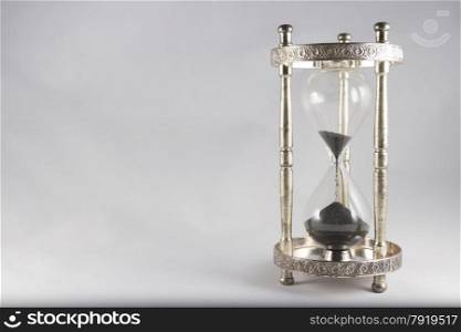 Antique hourglass, black sand, textured background. Right of image, blank space on left, landscape, top half almost empty.