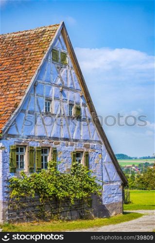 Antique house with German specific architecture, half timbered and stone walls of blue color, windows with wooden shutters and tile gable roof.