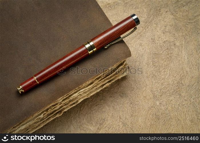 antique leather-bound journal or book with decked edge handmade paper pages and a stylish pen on a handmade bark paper, journaling concept
