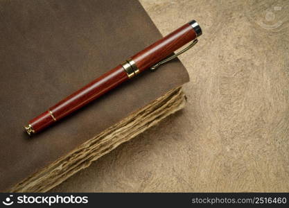 antique leather-bound journal or book with decked edge handmade paper pages and a stylish pen on a handmade bark paper, journaling concept