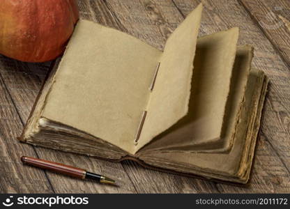 antique leatherbound journal with decked edge handmade paper pages and a stylish pen on a rustic wooden table with a small pumpkin, journaling concept