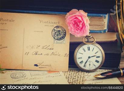 antique pocket  clock with postcard  on vintage  books and letters background, retro toned. antique clock on old  books and letters background