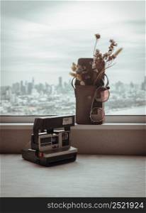 Antique polaroid camera, Sunglasses and Dried flowers in mini brown leather bag. Background it city and river view, Accessories and essential travel items, Vintage design, Selective focus.