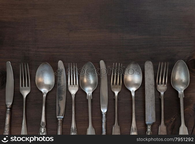 Antique silver cutlery in a row on old wooden background