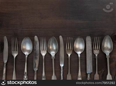 Antique silver cutlery in a row on old wooden background