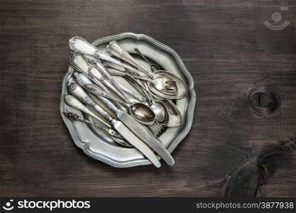 Antique silver cutlery on vintage tin plate on old wooden background