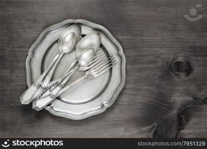Antique silver cutlery on vintage tin plate on old wooden background