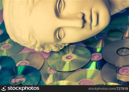 Antique statue of Venus head closeup against the background of glitter CDs. Concept of music, style, vintage. Toned.. Antique statue of Venus head close up on a glitter CDs background. Concept of music, style, vintage.