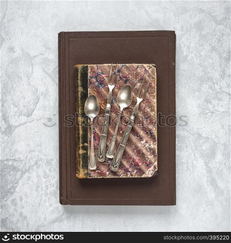 Antique teaspoons and dessert forks are on an old books