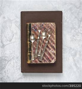 Antique teaspoons and dessert forks are on an old books