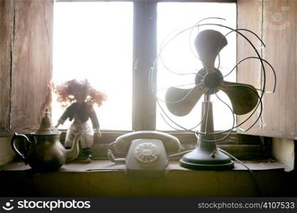 Antique vintage air fan, doll and phone at the window backlight