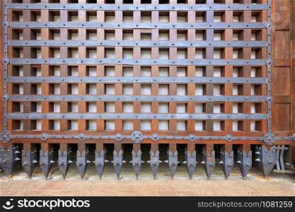 Antique wooden gates served as protection in antique castles and covered with a wrought-iron grille with serrated iron tips at the end.. Antique antique wooden gates are covered with forged bars and jagged tips at the end.