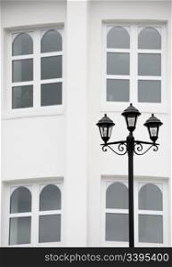 antiqued forged black street lamp against white wall with four arched windows