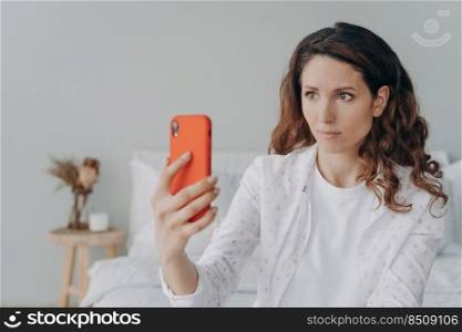 Anxious girl is looking at smartphone screen and reding message. Young pretty woman is chatting on phone at home. European girl in casual wear is texting and receiving calls.. Anxious girl is looking at smartphone screen. European girl is receiving messages on phone.