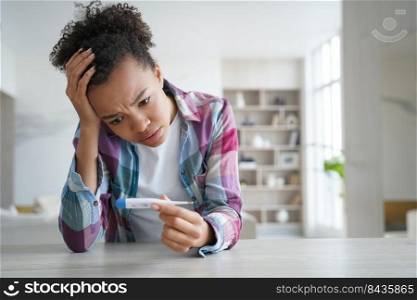 Anxious teenage girl gets positive pregnancy test result. Desperate african american young woman is holding stripe test and looking at it. Teenage lifestyle and mistakes. Contraception concept.. Anxious girl gets positive pregnancy test result. Young woman is holding stripe test.