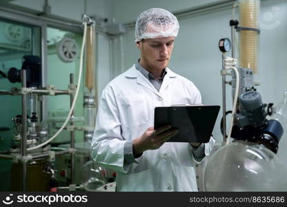 Apothecary scientist using a clipboard and pen to record information from a CBD oil extractor and a scientific machine used to create medicinal cannabis products.. Apothecary scientist recording data from CBD oil extractor in laboratory.