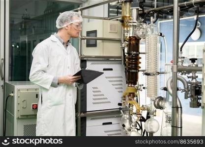 Apothecary scientist using a clipboard and pen to record information from a CBD oil extractor and a scientific machine used to create medicinal cannabis products.. Apothecary scientist recording data from CBD oil extractor in laboratory.