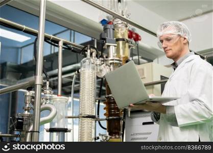 Apothecary scientist using laptop to record information from a CBD oil extractor and a scientific machine used to create medicinal cannabis products.. Apothecary scientist recording data from CBD oil extractor in laboratory.