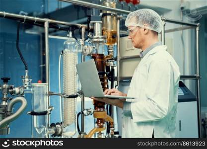 Apothecary scientist working with laptop near CBD oil extractor and a scientific machine used to create medicinal cannabis products.. Apothecary scientist working with laptop near CBD oil extractor in laboratory.
