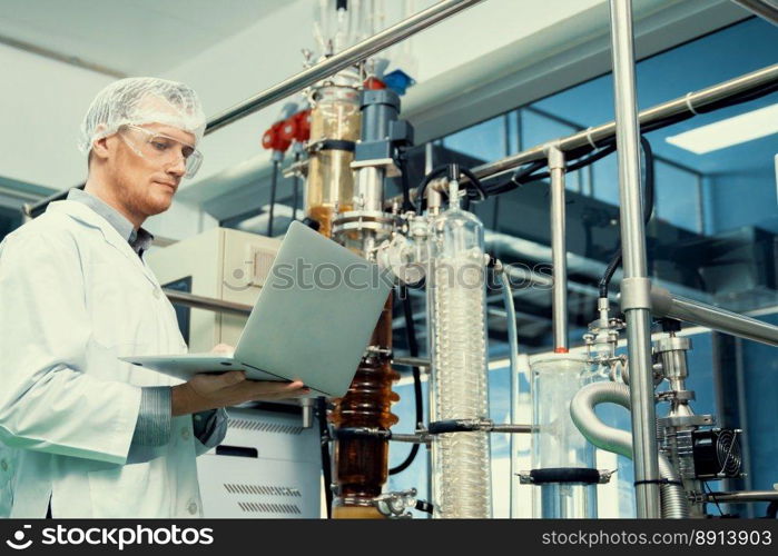 Apothecary scientist working with laptop near CBD oil extractor and a scientific machine used to create medicinal cannabis products.. Apothecary scientist working with laptop near CBD oil extractor in laboratory.