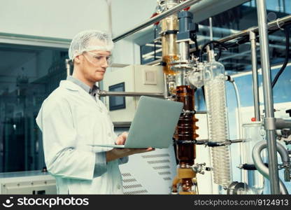 Apothecary scientist working with laptop near CBD oil extractor and a scientific machine used to create medicinal cannabis products.. Apothecary scientist working with laptop near CBD oil extractor in laboratory.