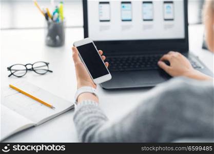 app design, technology and business concept - web designer or developer with smartphone and laptop computer working on user interface at office. web designer with smartphone and laptop at office