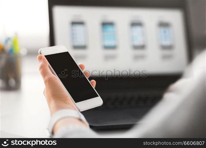 app design, technology and business concept - web designer or developer with smartphone and laptop computer working on user interface at office. web designer with smartphone and laptop at office
