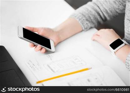 app design, technology and business concept - web designer or developer with smartphone, smart watch and sketch in notebook working on user interface at office. web designer creating mobile user interface