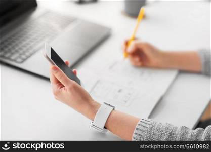 app design, technology and business concept - web designer or developer with smartphone working on user interface and drawing sketches at office. web designer working on smartphone user interface
