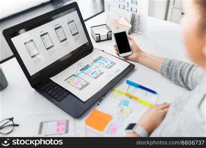 app design, technology and business people concept - web designer or developer with smartphone and laptop computer working on user interface at office. web designer with smartphone and laptop at office