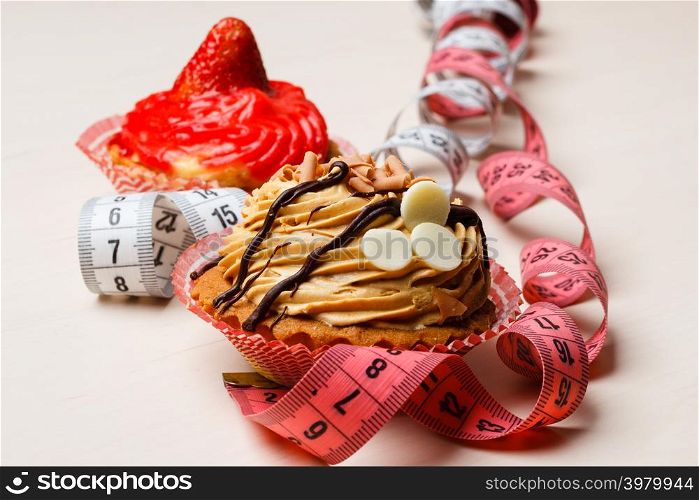 Appetite and gluttony concept. Fattening problem. Cakes cupcakes with measuring tapes on table
