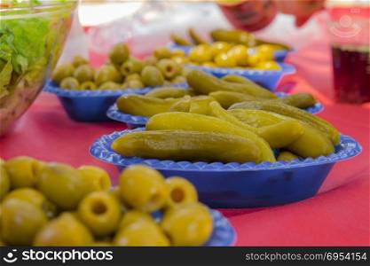 Appetizer food with pickled vegetables of cucumber and olives on picnic table.
