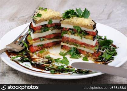 Appetizer from eggplant , slices of mozzarella combined in a pile with tomatoes spilled with herbs, seasoned Parmesan cheese. In section